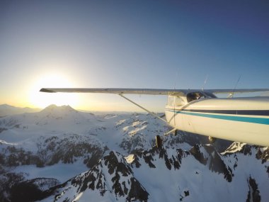 Canlı bir yaz gün batımı sırasında kayalık Kanada Dağları yakınında uçan küçük bir uçak. Squamish yakınlarında çekilmiş, Vancouver'ın kuzeyi, British Columbia, Kanada.