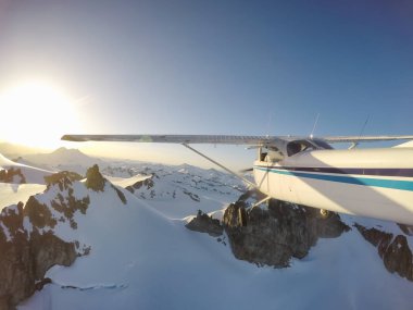 Canlı bir yaz gün batımı sırasında kayalık Kanada Dağları yakınında uçan küçük bir uçak. Squamish yakınlarında çekilmiş, Vancouver'ın kuzeyi, British Columbia, Kanada.