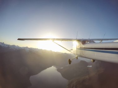 Canlı bir yaz gün batımı sırasında kayalık Kanada Dağları yakınında uçan küçük bir uçak. Squamish yakınlarında çekilmiş, Vancouver'ın kuzeyi, British Columbia, Kanada.