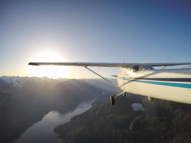 Canlı bir yaz gün batımı sırasında kayalık Kanada Dağları yakınında uçan küçük bir uçak. Squamish yakınlarında çekilmiş, Vancouver'ın kuzeyi, British Columbia, Kanada.