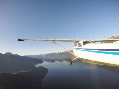 Canlı bir yaz gün batımı sırasında kayalık Kanada Dağları yakınında uçan küçük bir uçak. Squamish yakınlarında çekilmiş, Vancouver'ın kuzeyi, British Columbia, Kanada.