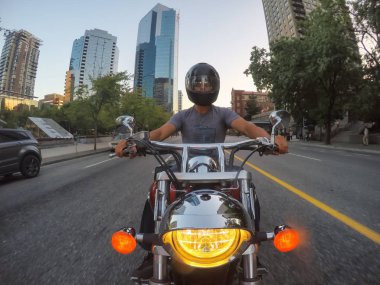 Downtown Vancouver, British Columbia, Canada - June 16, 2018: Man on a motorcycle is riding in a modern city during a sunny summer sunset. clipart