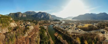 Aerial panoramic view of a small town with Chief Mountain in the background during a sunny day. Taken in Squamish, North of Vancouver, British Columbia, Canada. clipart