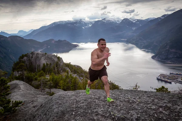 Fit and Muscular Young Man is Running up the Mountain during a cloudy day. Taken on Chief Mountain in Squamish, North of Vancouver, BC, Canada.