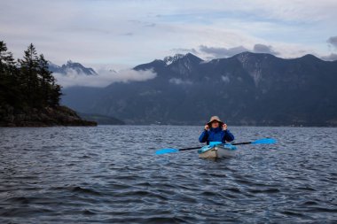 Kayıktaki maceracı adam bulutlu bir akşam da Howe Sound'da kürek çekiyor. Bowen Adası yakınlarında çekilen, Vancouver'ın kuzeybatısında, Bc, Kanada.