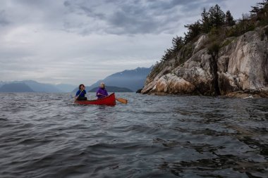 Kırmızı kano üzerinde çift maceracı kadın arkadaşlar bulutlu bir gün batımı sırasında Howe Sound kürek vardır. Horseshoe Bay, Batı Vancouver, Bc, Kanada.