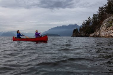 Kırmızı kano üzerinde çift maceracı kadın arkadaşlar bulutlu bir gün batımı sırasında Howe Sound kürek vardır. Horseshoe Bay, Batı Vancouver, Bc, Kanada.