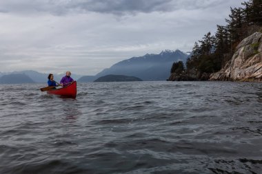 Kırmızı kano üzerinde çift maceracı kadın arkadaşlar bulutlu bir gün batımı sırasında Howe Sound kürek vardır. Horseshoe Bay, Batı Vancouver, Bc, Kanada.