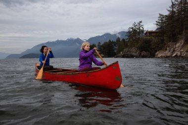 Kırmızı kano üzerinde çift maceracı kadın arkadaşlar bulutlu bir gün batımı sırasında Howe Sound kürek vardır. Horseshoe Bay, Batı Vancouver, Bc, Kanada.