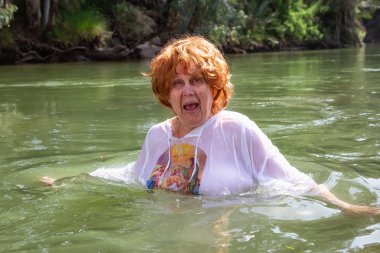 Yaşlı kadın İsrail'in kutsal topraklarında Ürdün Nehri'nde vaftiz ediliyor.