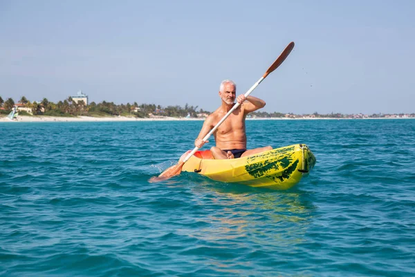 Elder fit man is kayaking on a bright yellow kayak in Caribbean Sea during a sunny summer day. Taken in Varadero, Cuba.