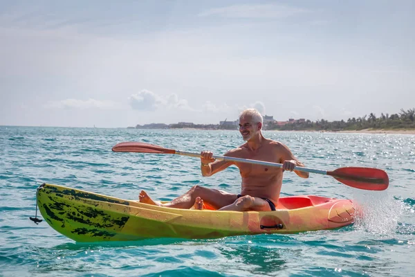 Elder fit man is kayaking on a bright yellow kayak in Caribbean Sea during a sunny summer day. Taken in Varadero, Cuba.