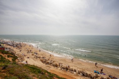 Tel Aviv, İsrail - 13 Nisan 2019: Bulutlu ve güneşli bir günde modern bir şehirde kalabalık bir plajın güzel manzarası.