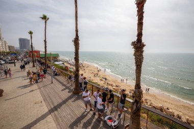 Tel Aviv, İsrail - 13 Nisan 2019: Bulutlu ve güneşli bir günde modern bir şehirde kalabalık bir plajın güzel manzarası.