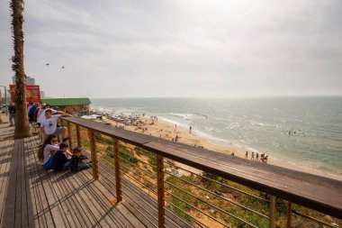 Tel Aviv, İsrail - 13 Nisan 2019: Bulutlu ve güneşli bir günde modern bir şehirde kalabalık bir plajın güzel manzarası.