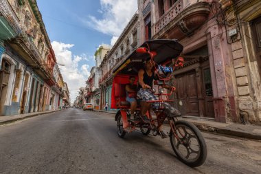 Havana, Küba - 14 Mayıs 2019: Canlı ve parlak güneşli bir sabahta Eski Havana Şehrinin sokaklarında bisikletli taksi şoförü.
