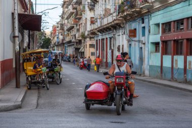 Havana, Küba - 13 Mayıs 2019: Canlı ve parlak güneşli bir günde Eski Havana Şehrinin sokaklarında motosikletsüren Kübalı adam.