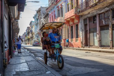 Havana, Küba - 13 Mayıs 2019: Canlı ve parlak güneşli bir sabahta Eski Havana Şehrinin sokaklarında bisikletli taksi şoförü.