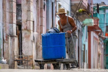 Havana, Küba - 17 Mayıs 2019: Yaşlı adam sıcak güneşli bir günde Eski Havana Şehrinin sokaklarında su dolu bir konteyner itiyor.