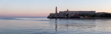 Renkli ve güneşli bir gün doğumu sırasında, Küba'nın başkenti Eski Havana'daki Deniz Feneri'nin panoramik manzarası.