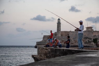 Havana, Küba - 25 Mayıs 2019: Küba halkı, Gıda Krizi Kıtlığı sırasında çekilen güneşli ve bulutlu gün doğumu sırasında sabahın erken saatlerinde okyanusta balık tutuyor.