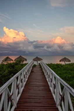 Bulutlu ve yağmurlu bir sabah gündoğumu sırasında Küba'da Karayip Denizi'nde kumlu plaja giden ahşap bir yol güzel görünümü.