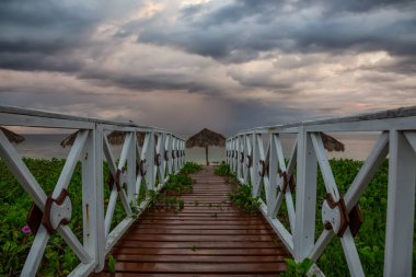 Bulutlu ve yağmurlu bir sabah gündoğumu sırasında Küba'da Karayip Denizi'nde kumlu plaja giden ahşap bir yol güzel görünümü.