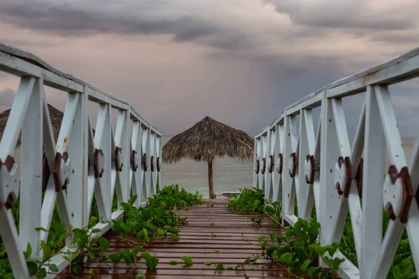 Beautiful view of a wooden path leading to the sandy beach on the Caribbean Sea in Cuba during a cloudy and rainy morning sunrise.