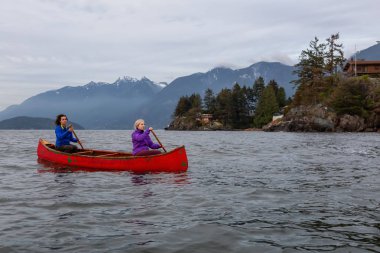 Kırmızı kano üzerinde çift maceracı kadın arkadaşlar bulutlu bir gün batımı sırasında Howe Sound kürek vardır. Horseshoe Bay, Batı Vancouver, Bc, Kanada.
