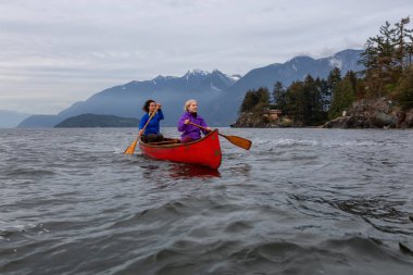Kırmızı kano üzerinde çift maceracı kadın arkadaşlar bulutlu bir gün batımı sırasında Howe Sound kürek vardır. Horseshoe Bay, Batı Vancouver, Bc, Kanada.