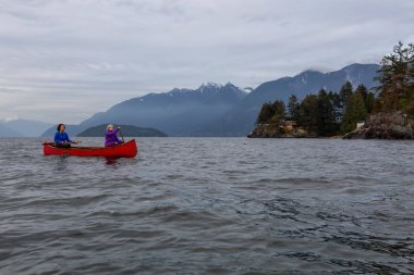 Kırmızı kano üzerinde çift maceracı kadın arkadaşlar bulutlu bir gün batımı sırasında Howe Sound kürek vardır. Horseshoe Bay, Batı Vancouver, Bc, Kanada.
