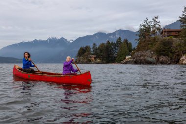 Kırmızı kano üzerinde çift maceracı kadın arkadaşlar bulutlu bir gün batımı sırasında Howe Sound kürek vardır. Horseshoe Bay, Batı Vancouver, Bc, Kanada.