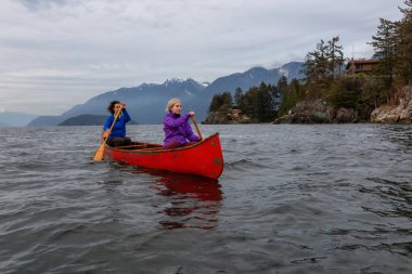 Kırmızı kano üzerinde çift maceracı kadın arkadaşlar bulutlu bir gün batımı sırasında Howe Sound kürek vardır. Horseshoe Bay, Batı Vancouver, Bc, Kanada.