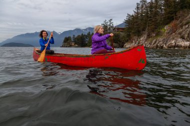 Kırmızı kano üzerinde çift maceracı kadın arkadaşlar bulutlu bir gün batımı sırasında Howe Sound kürek vardır. Horseshoe Bay, Batı Vancouver, Bc, Kanada.