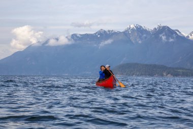 Kırmızı kano üzerinde çift maceracı kadın arkadaşlar bulutlu ve güneşli bir akşam boyunca Howe Sound kürek vardır. Bowen Adası yakınlarında çekilmiş, Vancouver'ın batısı, Bc, Kanada.