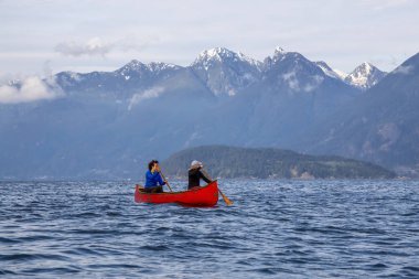 Kırmızı kano üzerinde çift maceracı kadın arkadaşlar bulutlu ve güneşli bir akşam boyunca Howe Sound kürek vardır. Bowen Adası yakınlarında çekilmiş, Vancouver'ın batısı, Bc, Kanada.