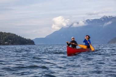 Kırmızı kano üzerinde çift maceracı kadın arkadaşlar bulutlu ve güneşli bir akşam boyunca Howe Sound kürek vardır. Bowen Adası yakınlarında çekilmiş, Vancouver'ın batısı, Bc, Kanada.