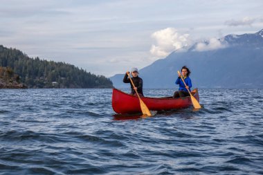 Kırmızı kano üzerinde çift maceracı kadın arkadaşlar bulutlu ve güneşli bir akşam boyunca Howe Sound kürek vardır. Bowen Adası yakınlarında çekilmiş, Vancouver'ın batısı, Bc, Kanada.
