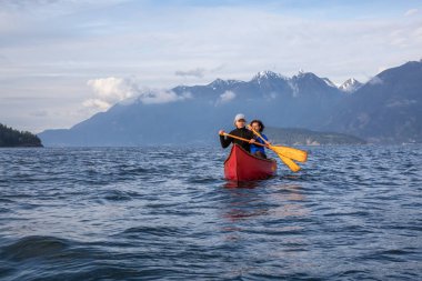 Kırmızı kano üzerinde çift maceracı kadın arkadaşlar bulutlu ve güneşli bir akşam boyunca Howe Sound kürek vardır. Bowen Adası yakınlarında çekilmiş, Vancouver'ın batısı, Bc, Kanada.