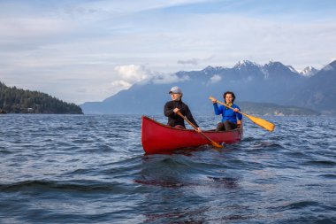 Kırmızı kano üzerinde çift maceracı kadın arkadaşlar bulutlu ve güneşli bir akşam boyunca Howe Sound kürek vardır. Bowen Adası yakınlarında çekilmiş, Vancouver'ın batısı, Bc, Kanada.