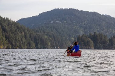 Kırmızı kano üzerinde çift maceracı kadın arkadaşlar bulutlu ve güneşli bir akşam boyunca Howe Sound kürek vardır. Bowen Adası yakınlarında çekilmiş, Vancouver'ın batısı, Bc, Kanada.