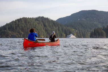 Kırmızı kano üzerinde çift maceracı kadın arkadaşlar bulutlu ve güneşli bir akşam boyunca Howe Sound kürek vardır. Bowen Adası yakınlarında çekilmiş, Vancouver'ın batısı, Bc, Kanada.