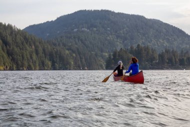 Kırmızı kano üzerinde çift maceracı kadın arkadaşlar bulutlu ve güneşli bir akşam boyunca Howe Sound kürek vardır. Bowen Adası yakınlarında çekilmiş, Vancouver'ın batısı, Bc, Kanada.