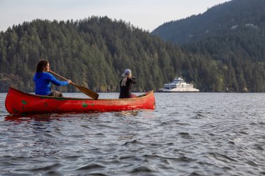 Kırmızı kano üzerinde maceracı arkadaşlar bulutlu bir gün boyunca arka planda Ferry Boat ile Howe Sound kürek vardır. Bowen Adası yakınlarında çekilmiş, Vancouver'ın batısı, Bc, Kanada.