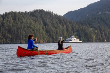 Kırmızı kano üzerinde maceracı arkadaşlar bulutlu bir gün boyunca arka planda Ferry Boat ile Howe Sound kürek vardır. Bowen Adası yakınlarında çekilmiş, Vancouver'ın batısı, Bc, Kanada.
