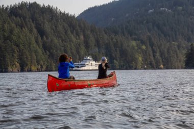 Kırmızı kano üzerinde maceracı arkadaşlar bulutlu bir gün boyunca arka planda Ferry Boat ile Howe Sound kürek vardır. Bowen Adası yakınlarında çekilmiş, Vancouver'ın batısı, Bc, Kanada.