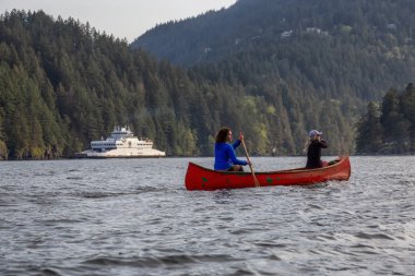 Kırmızı kano üzerinde maceracı arkadaşlar bulutlu bir gün boyunca arka planda Ferry Boat ile Howe Sound kürek vardır. Bowen Adası yakınlarında çekilmiş, Vancouver'ın batısı, Bc, Kanada.
