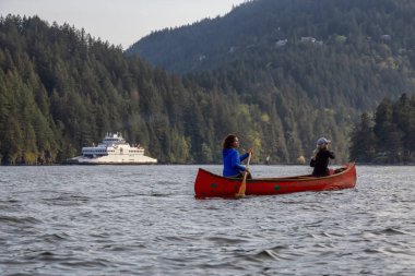 Kırmızı kano üzerinde maceracı arkadaşlar bulutlu bir gün boyunca arka planda Ferry Boat ile Howe Sound kürek vardır. Bowen Adası yakınlarında çekilmiş, Vancouver'ın batısı, Bc, Kanada.