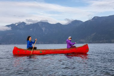 Kırmızı kano üzerinde çift maceracı kadın arkadaşlar bulutlu bir gün batımı sırasında Howe Sound kürek vardır. Bowen Adası yakınlarında çekilmiş, Vancouver'ın batısı, Bc, Kanada.