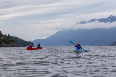 Kırmızı kano ve kano üzerinde maceracı arkadaşlar bulutlu bir gün batımı sırasında Howe Sound kürek vardır. Bowen Adası yakınlarında çekilmiş, Vancouver'ın batısı, Bc, Kanada.